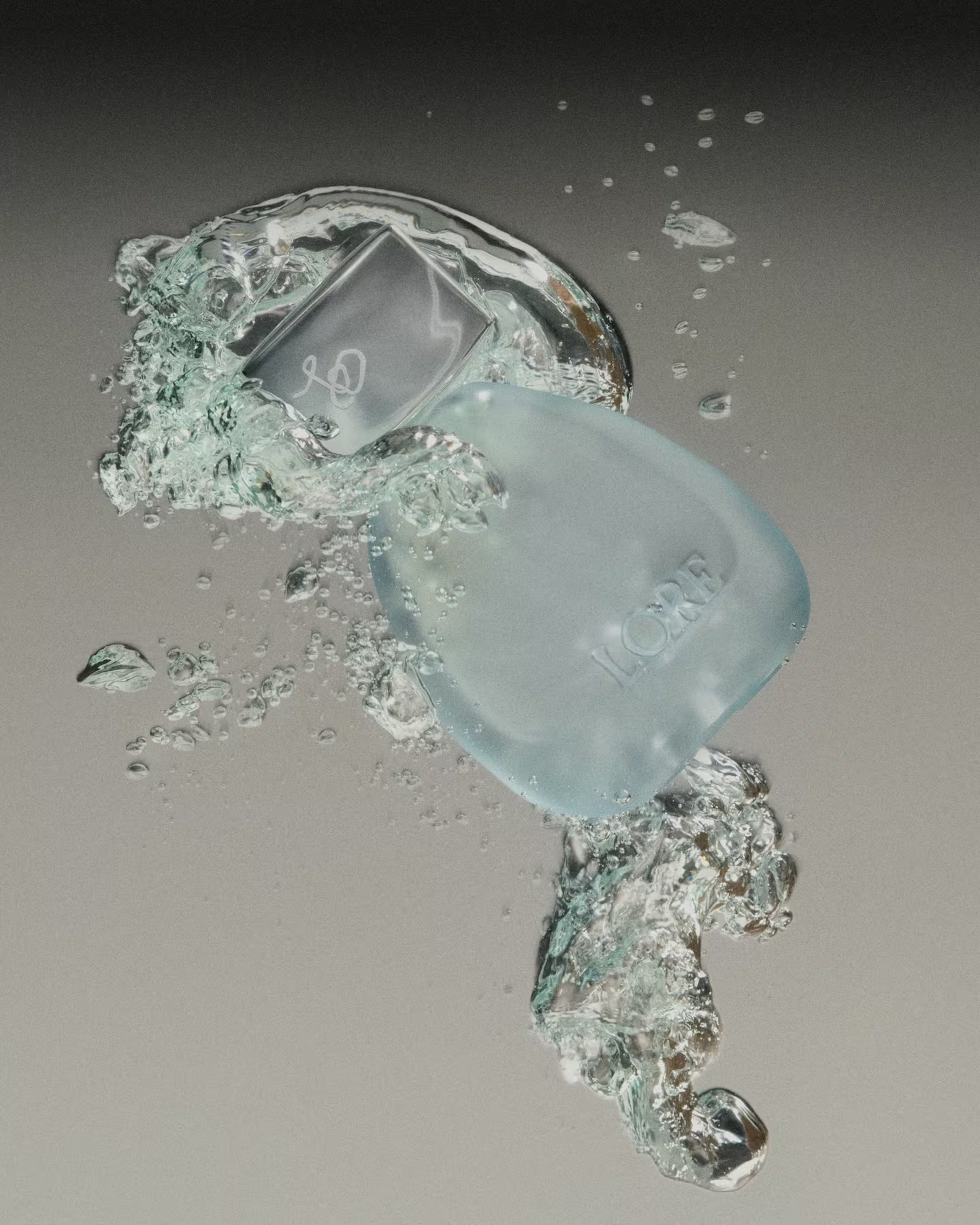 Clear glass perfume bottle caught in a splash of water against a grey backdrop